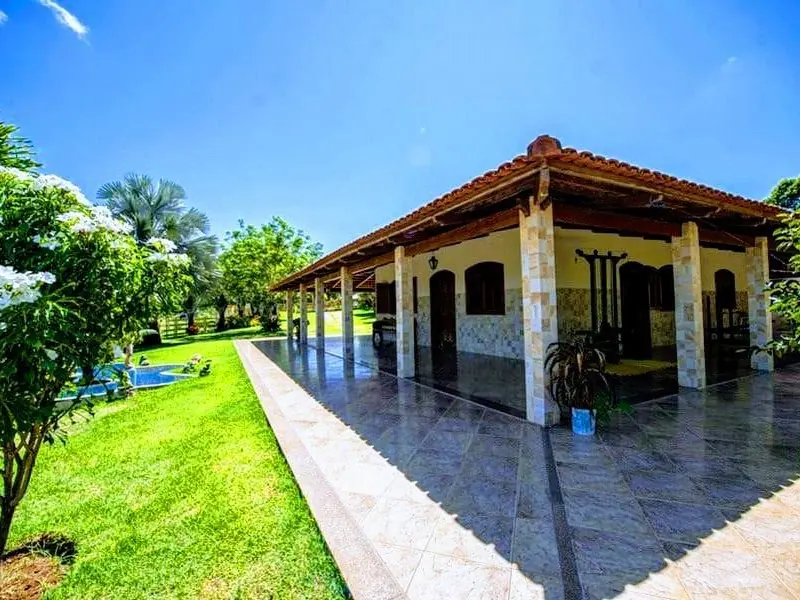 Casa térrea de telhado cerâmico com varanda de piso escuro e pilares revestidos de pedra, ao lado de um gramado